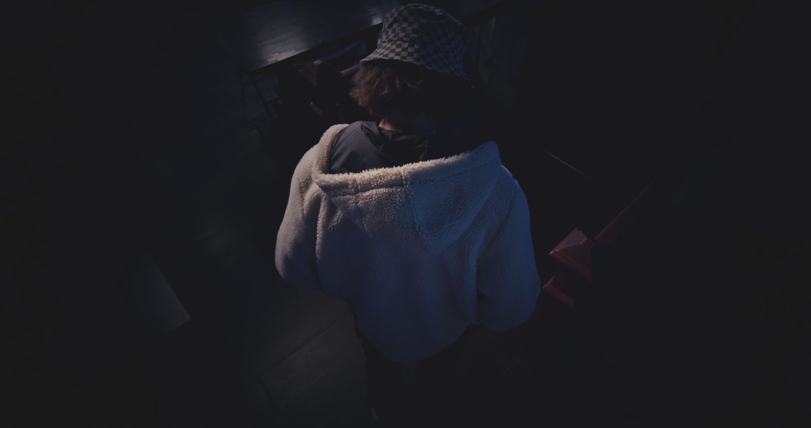 A figure curled on the floor in near darkness, wrapped in a blue sleeve.