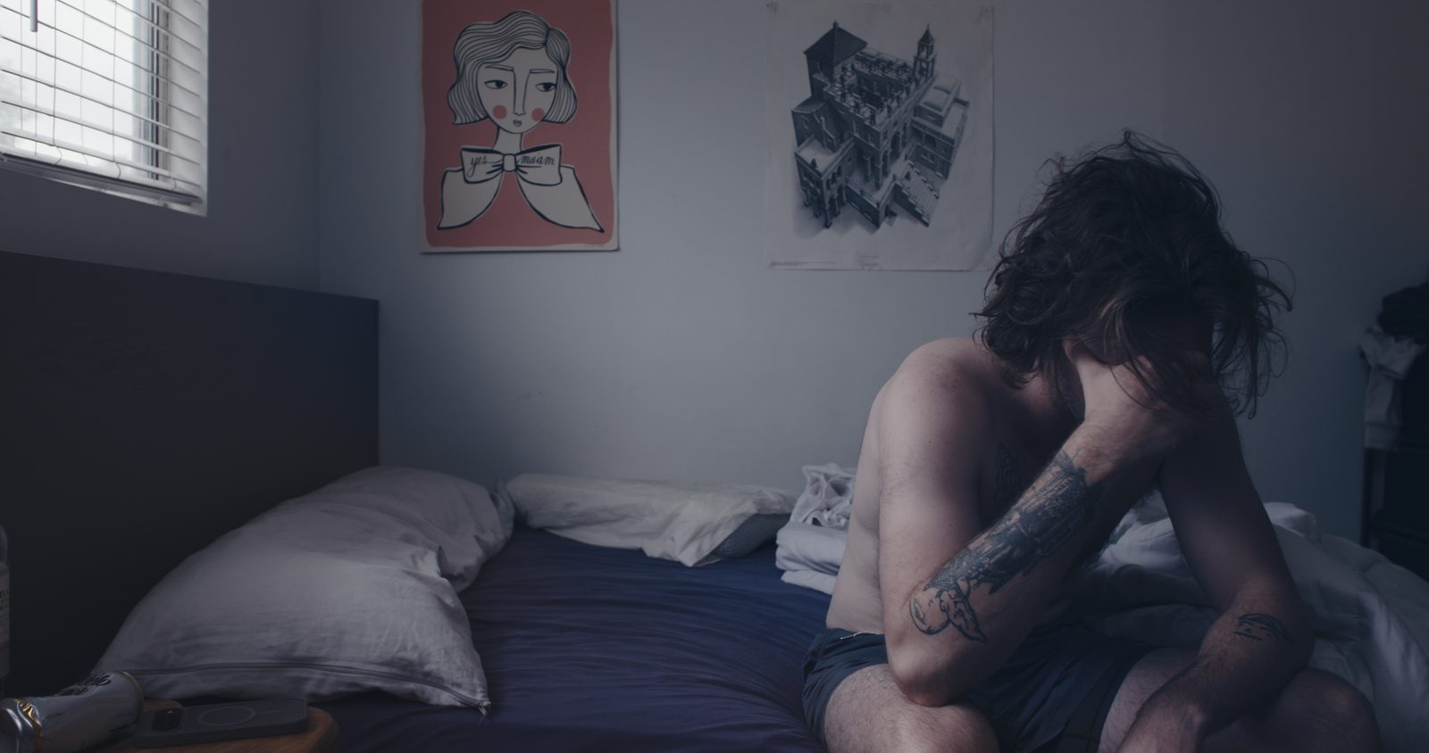A man sitting on the edge of a bed with his head in his hands.
