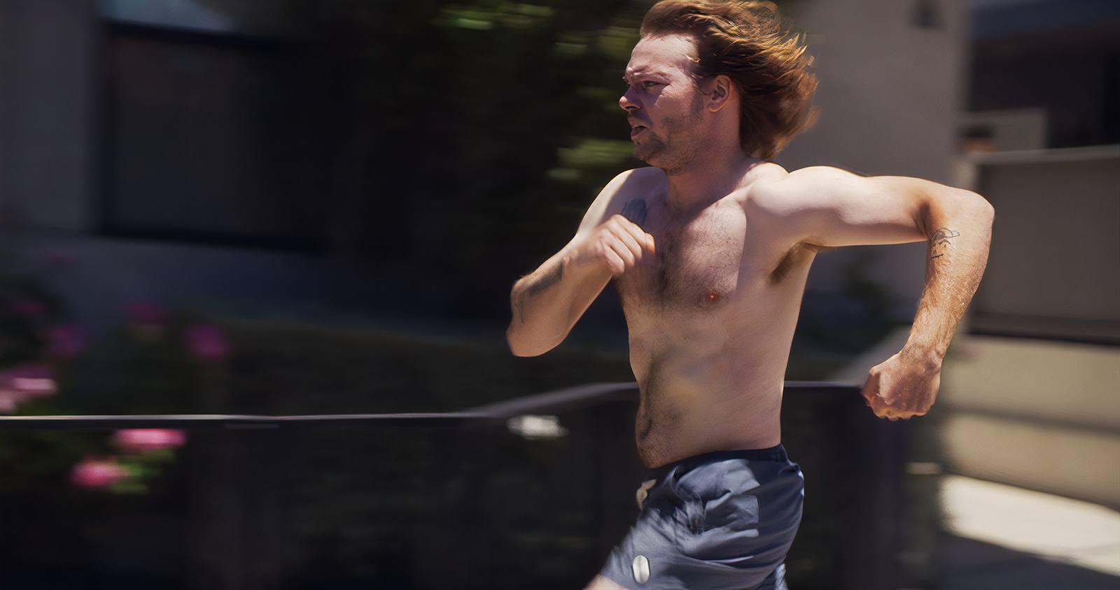 The same man running, seen closer and from the side, sunlit against a wall.